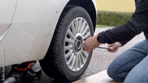 A male person grabbing a socket wrench to losen the bults on the summer tyres on his car, getting ready to change to winter tyres. Filmed in slow motion, no camera movements. photo