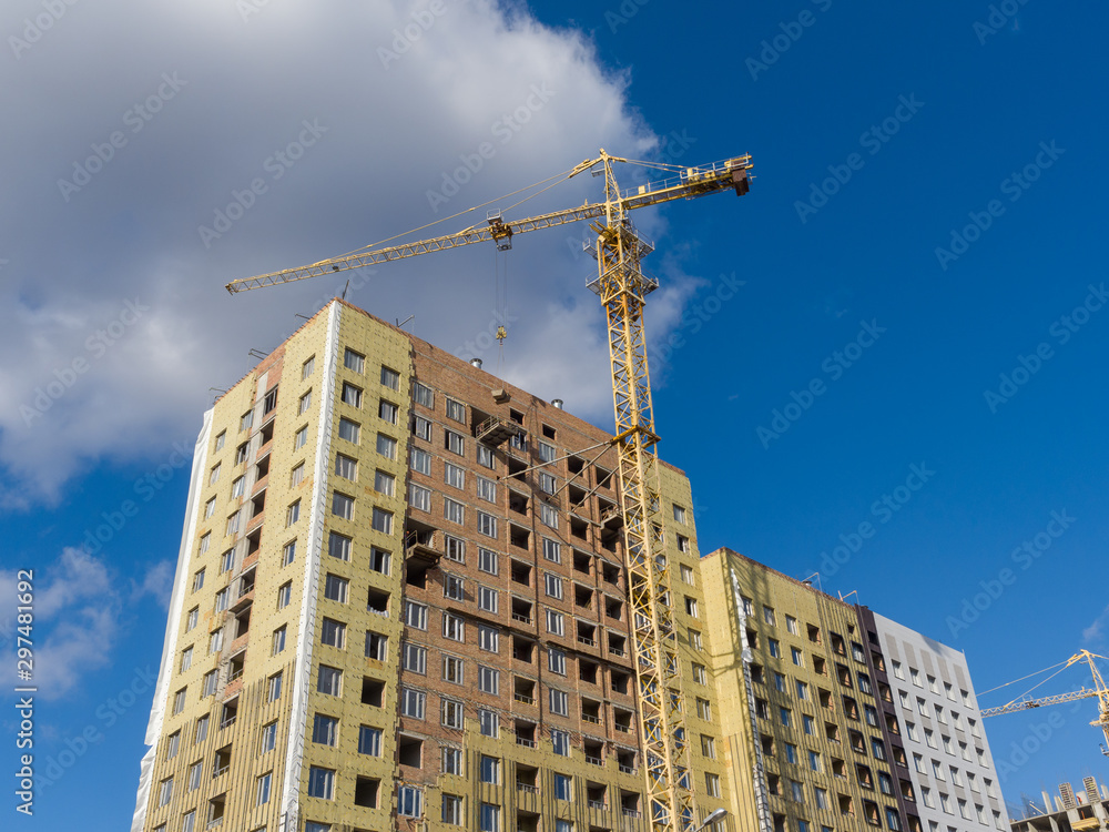 Fototapeta premium A tower crane is building a high-rise apartment building of brick. The walls are insulated. The theme of an emerging housing market under construction