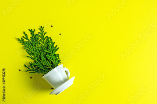Creative Christmas tree. Fluffy green sprigs in a white coffee cup on a yellow background. Save the space, New Year holidays, congratulations, background for creativity