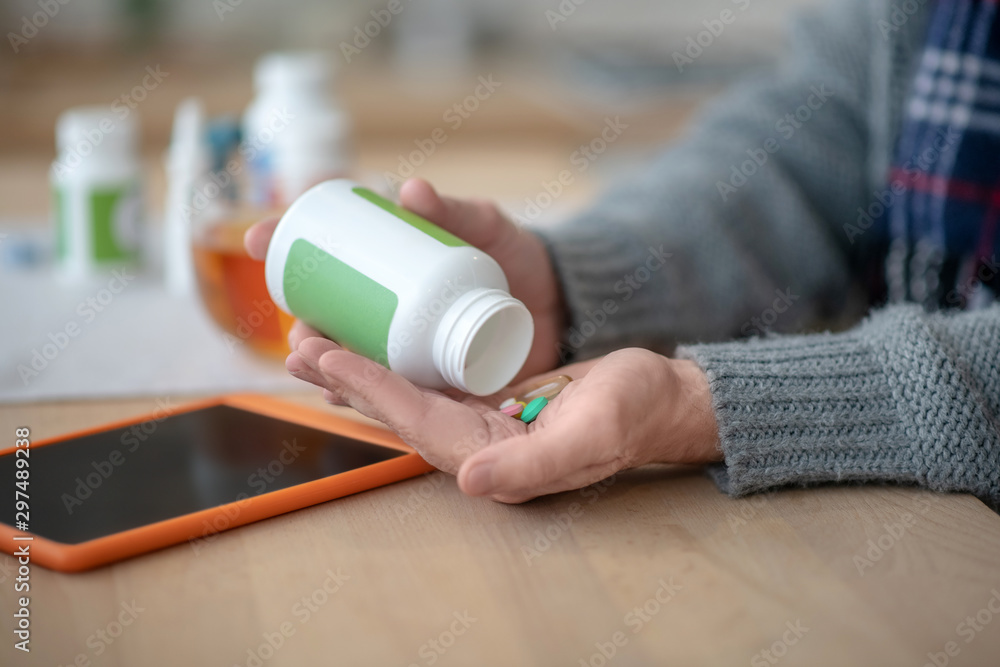 Close up of man taking pills after reading news on tablet