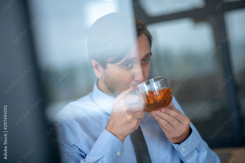 Blue-eyed businessman drinking hot tea at work