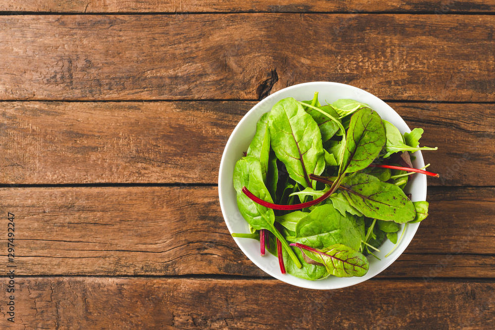 Overhead shot of fresh green salad with spinach, arugula and beetroot leaves in bowl on old wooden background with copyspace Overhead shot of fresh green salad with spinach, arugula and beetroot leaves in bowl on old wooden background with copyspace