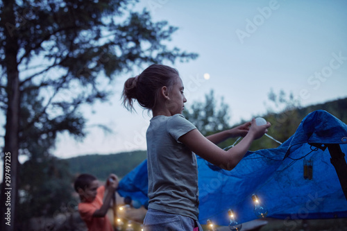 Kids making a small tent with candles and lampions in the backyard. © astrosystem