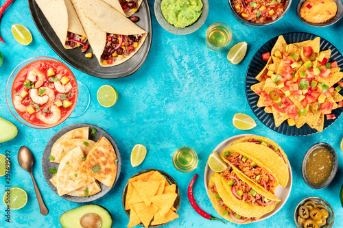 Mexican food, many dishes of the cuisine of Mexico, flat lay, shot from the top on a vibrant blue background, forming a frame with a place for text. Nachos, quesadillas, guacamole, burritos etc photo