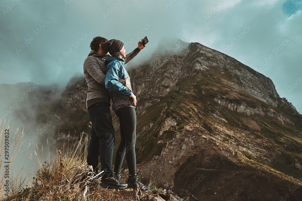 a young, happy couple hugges on a cliff and takes a selfi photo