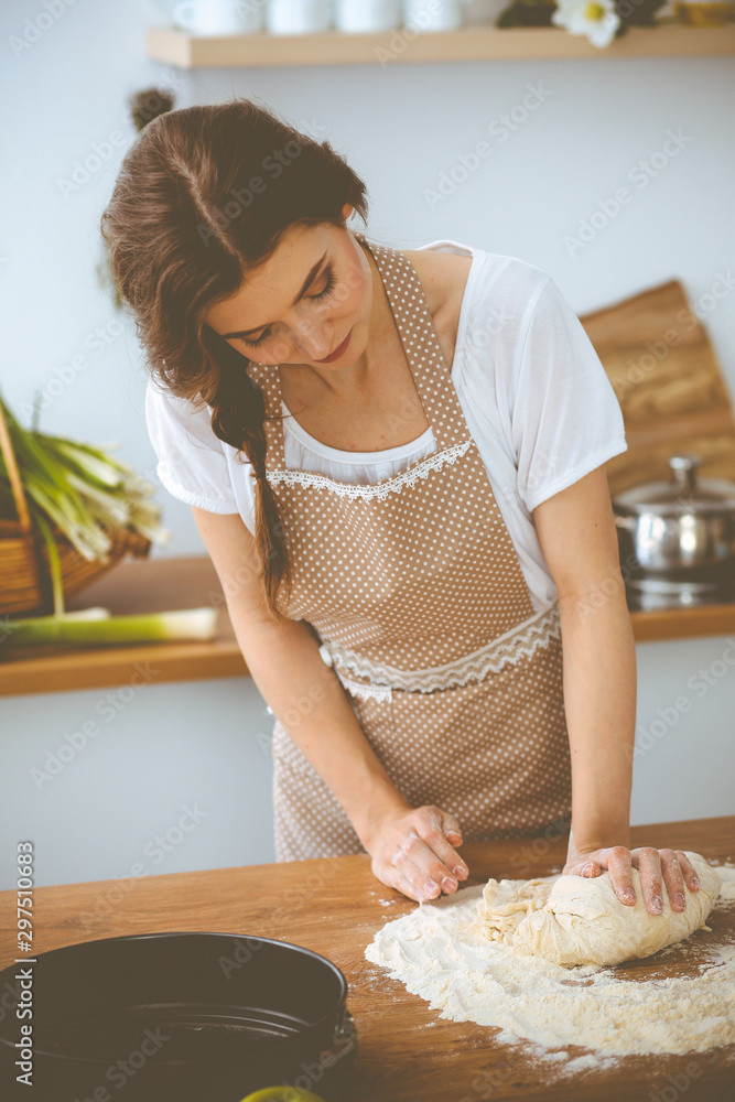Young brunette woman cooking pizza or handmade pasta in the kitchen. Housewife preparing dough on wooden table. Dieting, food and health concept Young brunette woman cooking pizza or handmade pasta in the kitchen. Housewife preparing dough on wooden table. Dieting, food and health concept