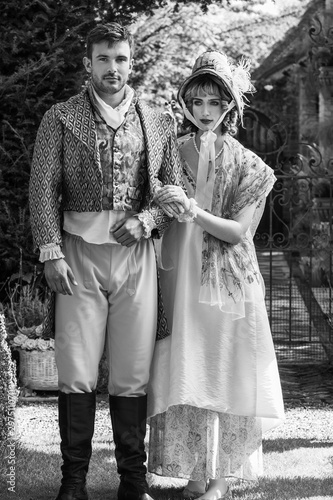 Potrait of young attractive couple dressed in vintage clothing walking through garden arm in arm