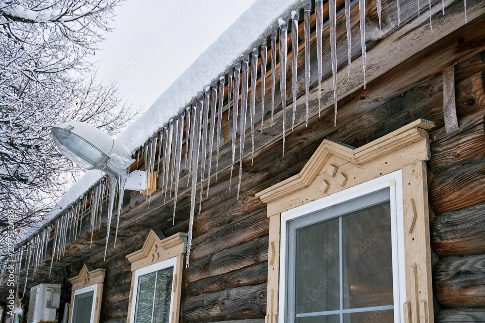 Large dangerous icicles hanging on the roof of a wooden country house in winter or spring in Russia.
