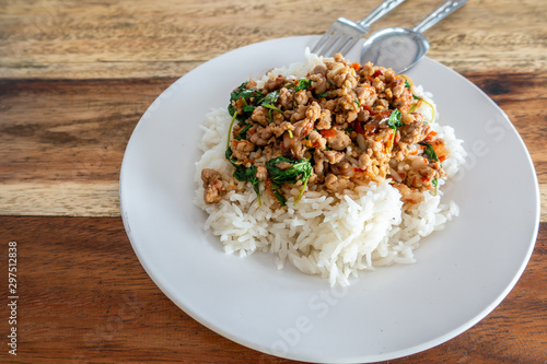 Rice topped with stir-fried pork and basil in  white dish on wooden table. , Text space.