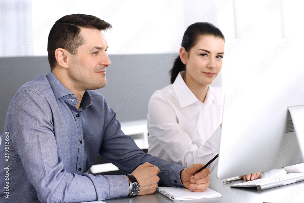 Obraz premium Cheerful smiling businessman and woman working with computer in modern office. Headshot at meeting or workplace. Teamwork, partnership and business concept