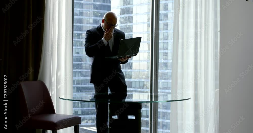 male lawyer is working in his office, standing near window and holding open laptop in hands male lawyer is working in his office, standing near window and holding open laptop in hands