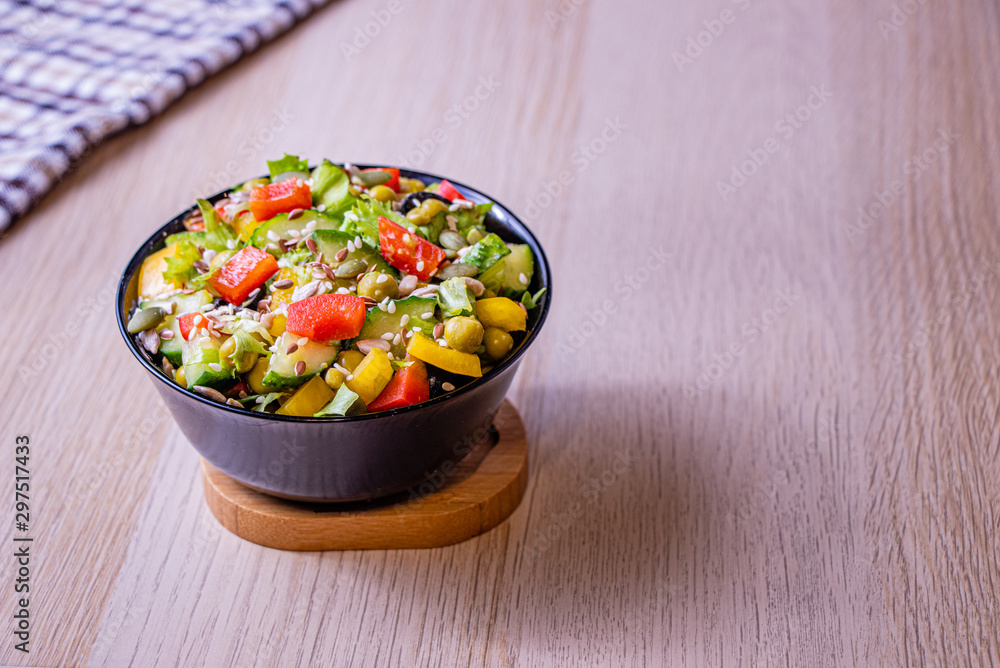 Vegetable salad in a dark bowl on a light background. Green Leaf Lettuce, cucumber, bell pepper, green peas, black and green olives, sprinkled with sunflower seeds, pumpkin seeds, sesame seeds. Vegetable salad in a dark bowl on a light background. Green Leaf Lettuce, cucumber, bell pepper, green peas, black and green olives, sprinkled with sunflower seeds, pumpkin seeds, sesame seeds.