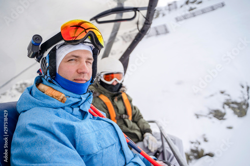 Photo of two snowboarders in helmet and mask on cable car