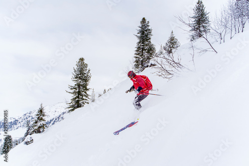 Side photo of sports man in red jacket and with backpack skiing in winter resort