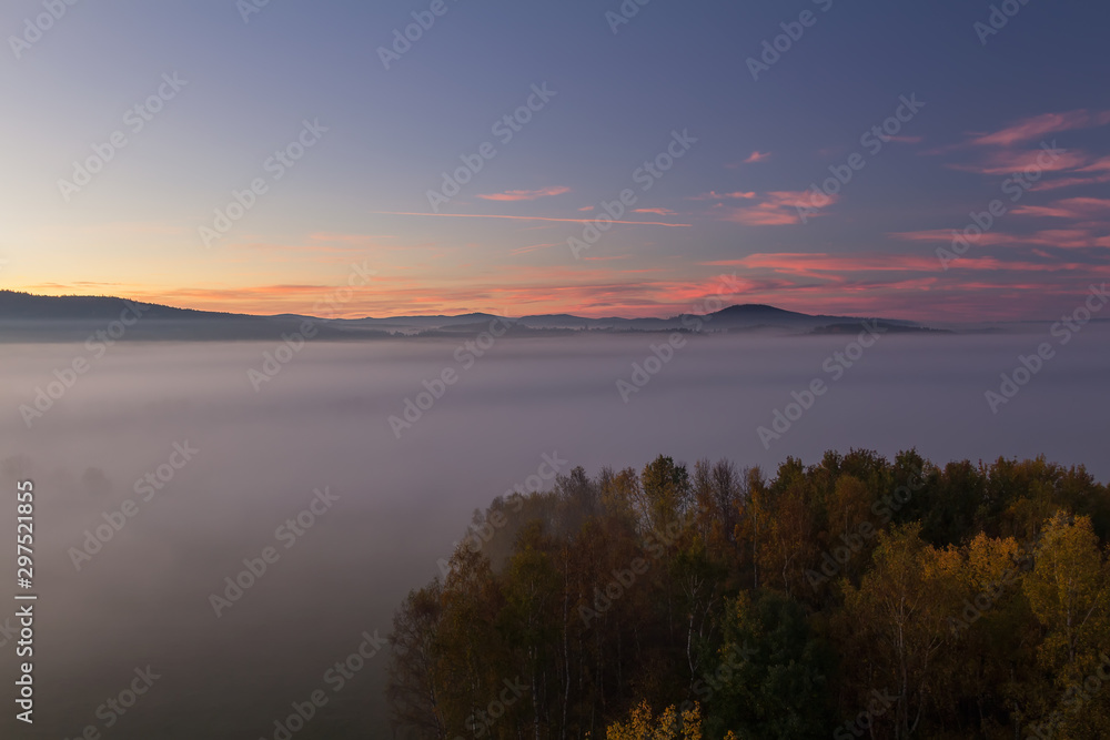 Aerial view to autumn misty fog, trees and hill in sunrise, Czech landscape