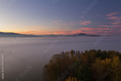 Aerial view to autumn misty fog, trees and hill in sunrise, Czech landscape