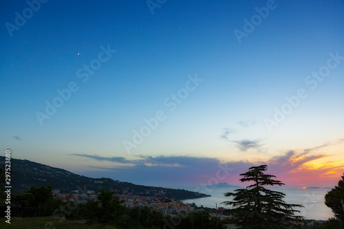 The crescent moon rises over Sorrento, a town overlooking the Bay of Naples in Southern Italy as the sun sets below the horizon.