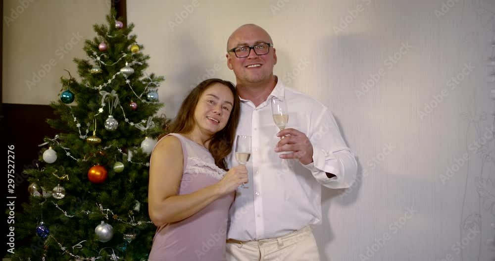 happy married couple is embracing, holding glasses with champagne in room with Christmas tree happy married couple is embracing, holding glasses with champagne in room with Christmas tree