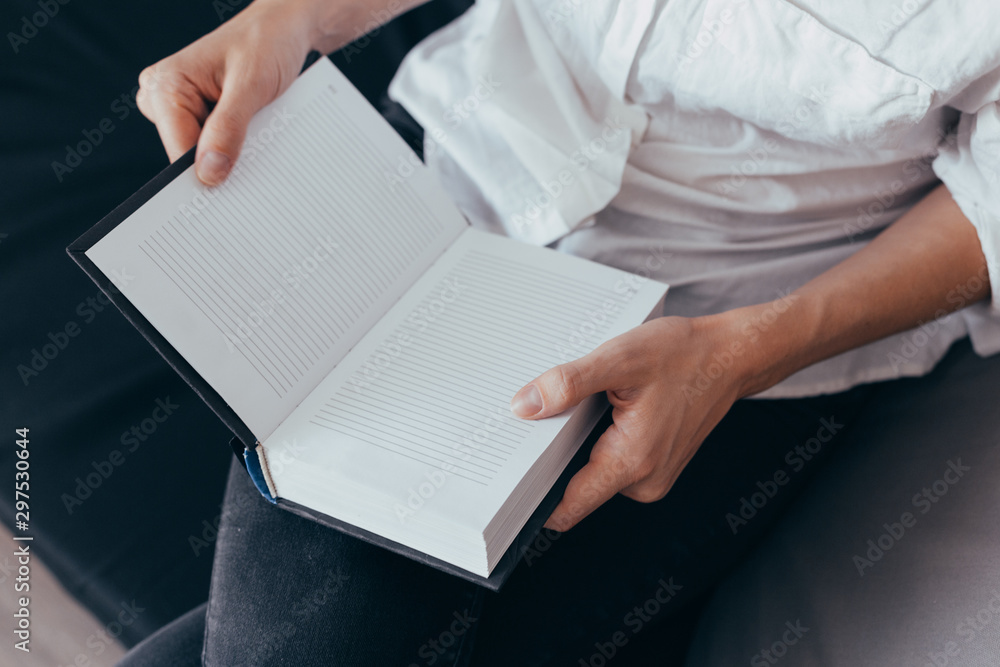 Beautiful female hands hold an open book or magazine in the room Beautiful female hands hold an open book or magazine in the room