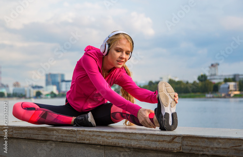Pretty girl wearing sportswear and doing stretching exercises on windy day at quay. photo