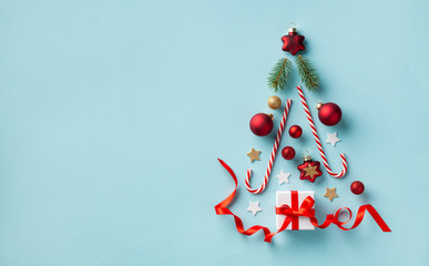 Creative Christmas fir tree made of gift box and holiday decorations on blue background top view. New Year greeting card. Flat lay.