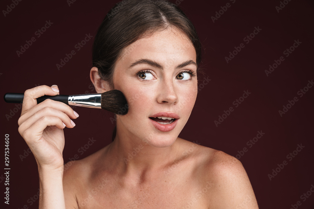 Image of young half-naked woman looking aside and using makeup brush Image of young half-naked woman looking aside and using makeup brush