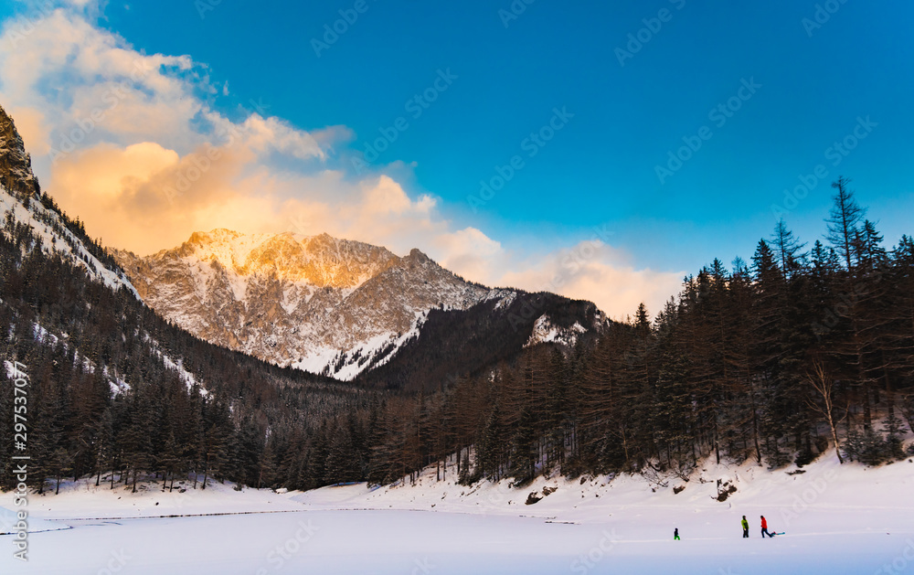 Peaceful mountain view at green lake. Frozen lake in winter during sunset with mountain peak in background.