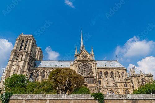 Lovely panoramic side view of the south façade of the famous medieval Notre-Dame cathedral on the Île de la Cité in Paris on a nice summer day with blue sky. The huge rose window stands out.