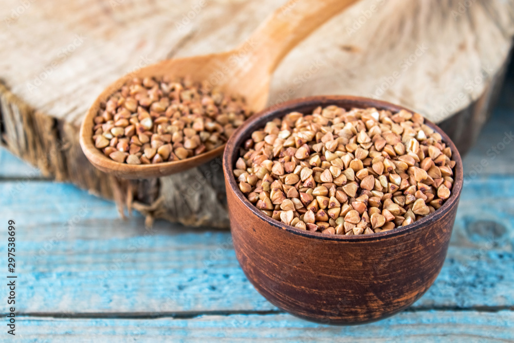 Uncooked buckwheat in a bowl on old blue boards. Buckwheat is used for cooking. Uncooked buckwheat in a bowl on old blue boards. Buckwheat is used for cooking.