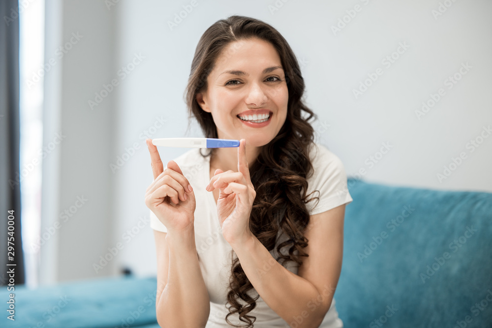 young beautiful woman sits on the sofa holding pregnancy test feeling happy young beautiful woman sits on the sofa holding pregnancy test feeling happy