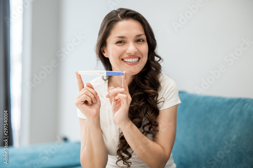 young beautiful woman sits on the sofa holding pregnancy test feeling happy