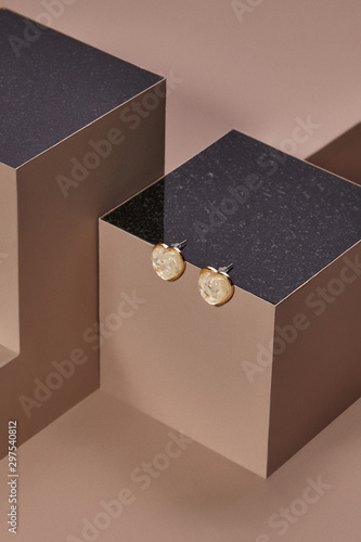 Object photo of a heart earrings, located on a dark beige cube with black marble upper side. The space around cube is polyformed.  photo