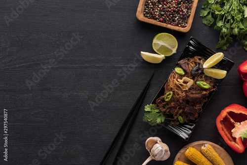 top view of tasty spicy thai noodles near chopsticks and fresh ingredients on wooden grey surface
