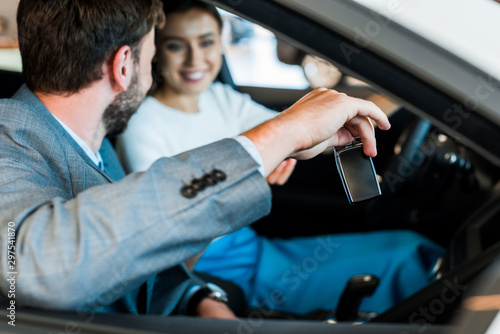 selective focus of bearded man holding car key near smiling woman sitting in car