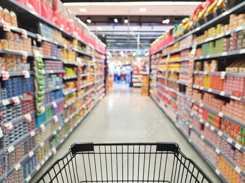 Supermarket aisle with empty shopping cart with customer defocus background photo