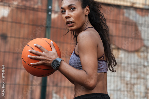 Image of african american woman playing basketball at playground outdoors photo