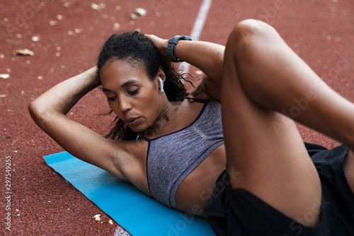 Image of african american woman doing criss cross crunches at mat outdoors