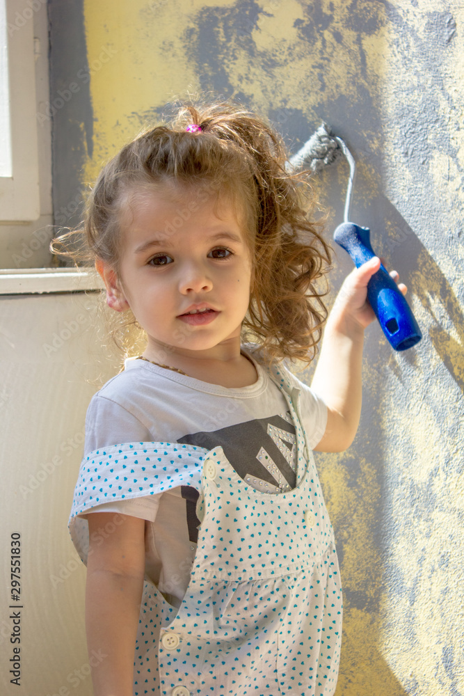 Fototapeta premium Little kid girl paints wall by paint roller