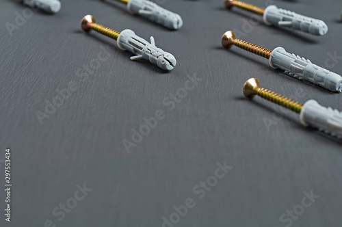 Rows of many new useful plastic gray dowel with glossy screw golden color for fixing different predmet on wall lies on scratches dark concrete table in workshop. Space for text