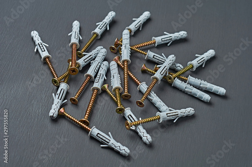 Scattered many new plastic gray dowel with glossy screw golden color for fixing different predmet on wall lies on scratches dark concrete table in workshop. Close-up photo