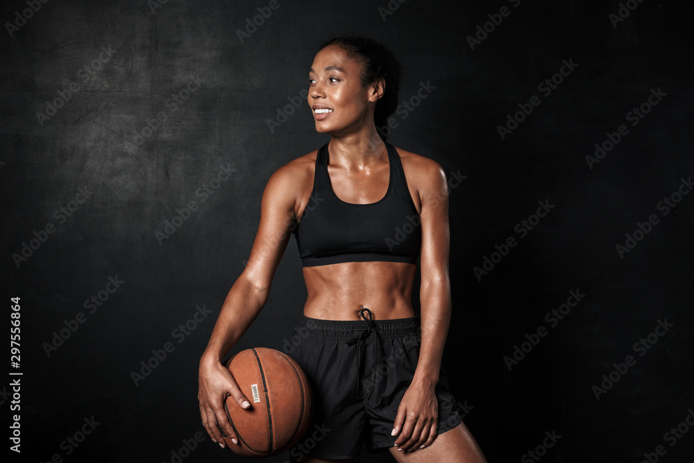 Image of smiling african american woman in sportswear holding basketball - obrazy, fototapety, plakaty 
