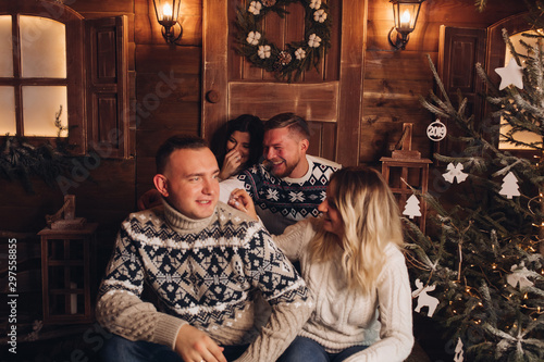 Two married couples are friends. Together celebrate the New Year. Celebrate Christmas. Champagne in the hands of girls and boys. Against the background of a wooden house. Cozy atmosphere © Вячеслав Косько