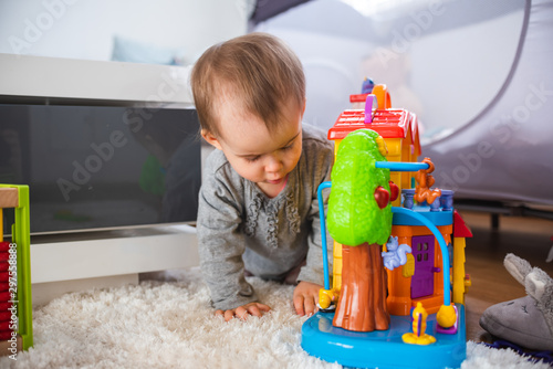 Cute little baby playing with toys in living room on a carpet floor.