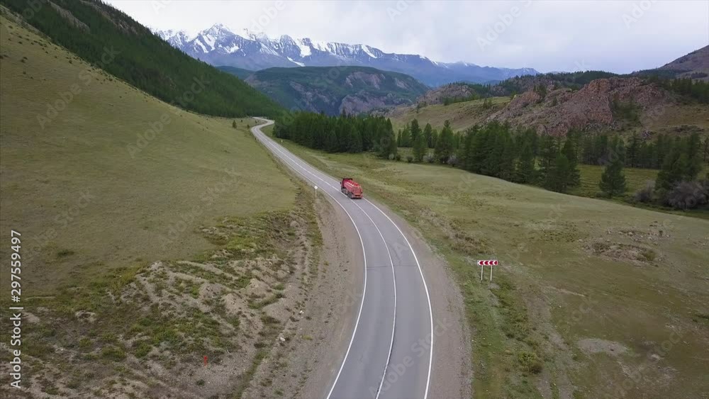 Flight over the asphalt road in mountains with red truck moving on it Flight over the asphalt road in mountains with red truck moving on it