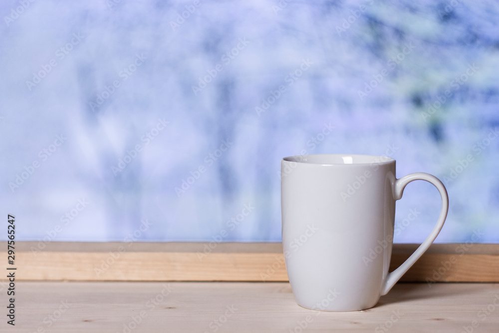 White cup on wooden background at window with blurred snow landscape. Winter comfort concept. White cup on wooden background at window with blurred snow landscape. Winter comfort concept.