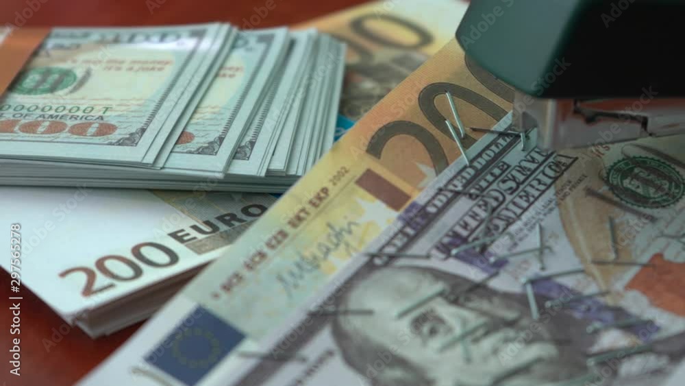 The stapler fastens the dollar and euro notes with iron clips. Stapler with paper clips on the background of banknotes. Counterfeit money The stapler fastens the dollar and euro notes with iron clips. Stapler with paper clips on the background of banknotes. Counterfeit money