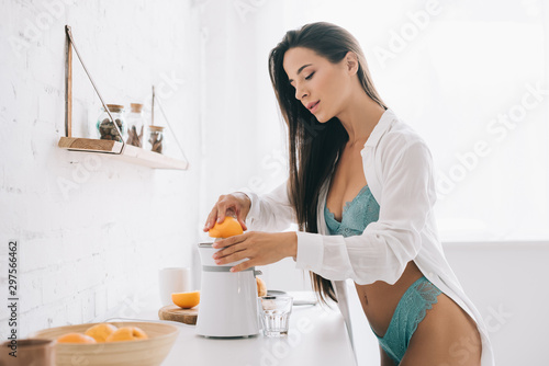 beautiful woman in lingerie making orange juice with citrus squeezer on kitchen photo