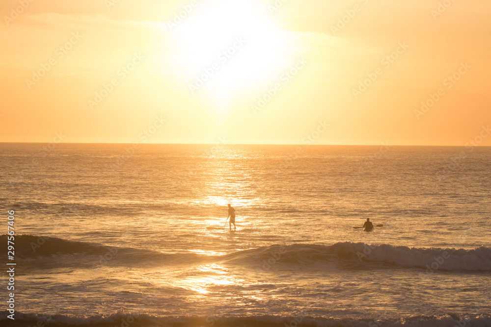 Golden Orange Sunrise With Waves Crashing And People On Kayaks And Paddle Boards In The Distance With Salt Spray In The Air
