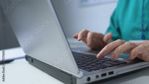 Aged medical worker typing on laptop, recording patient data in online register