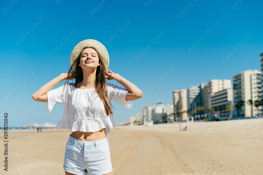 girl throws back her head in pleasure, holds her hat on the beach with her hands on a sunny day girl throws back her head in pleasure, holds her hat on the beach with her hands on a sunny day